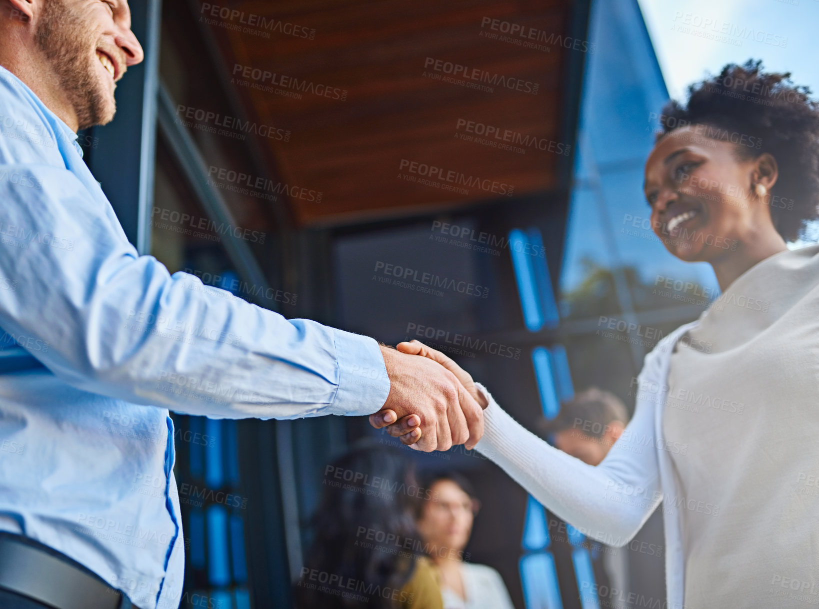 Buy stock photo Cropped shot of two businesspeople shaking hands with their coworkers in the background
