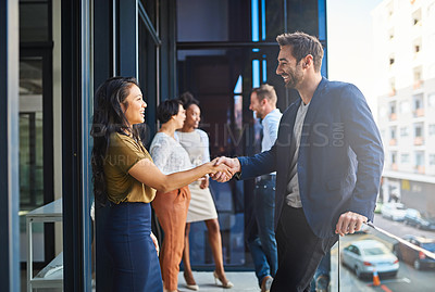 Buy stock photo Cropped shot of two businesspeople shaking hands on a balcony with their coworkers in the background