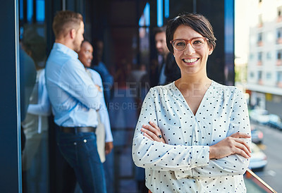 Buy stock photo Portrait of a young businesswoman standing on a balcony with her arms crossed and her coworkers in the background