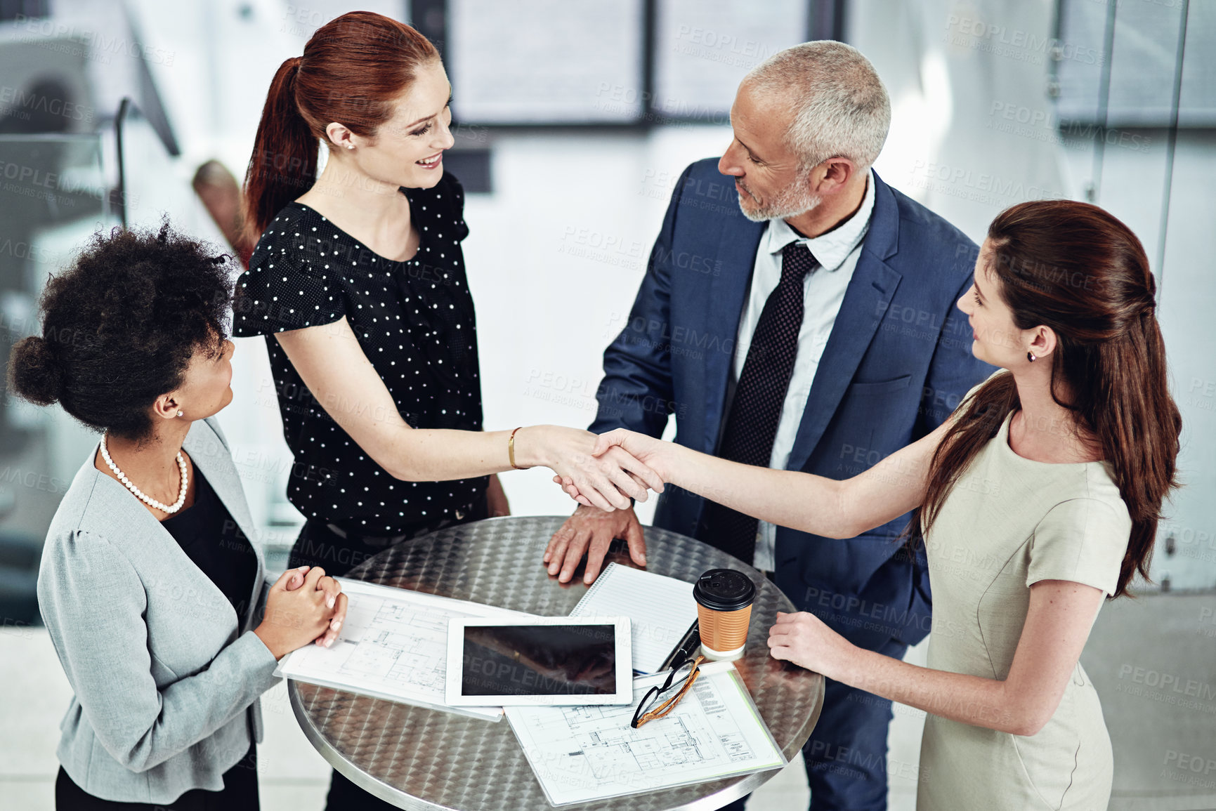 Buy stock photo Shot of two businesswomen shaking hands during a team meeting at work