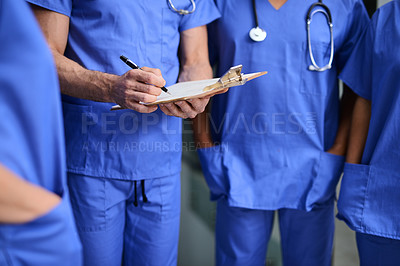 Buy stock photo Cropped shot of a medical practitioner writing notes on a clipboard with colleagues around