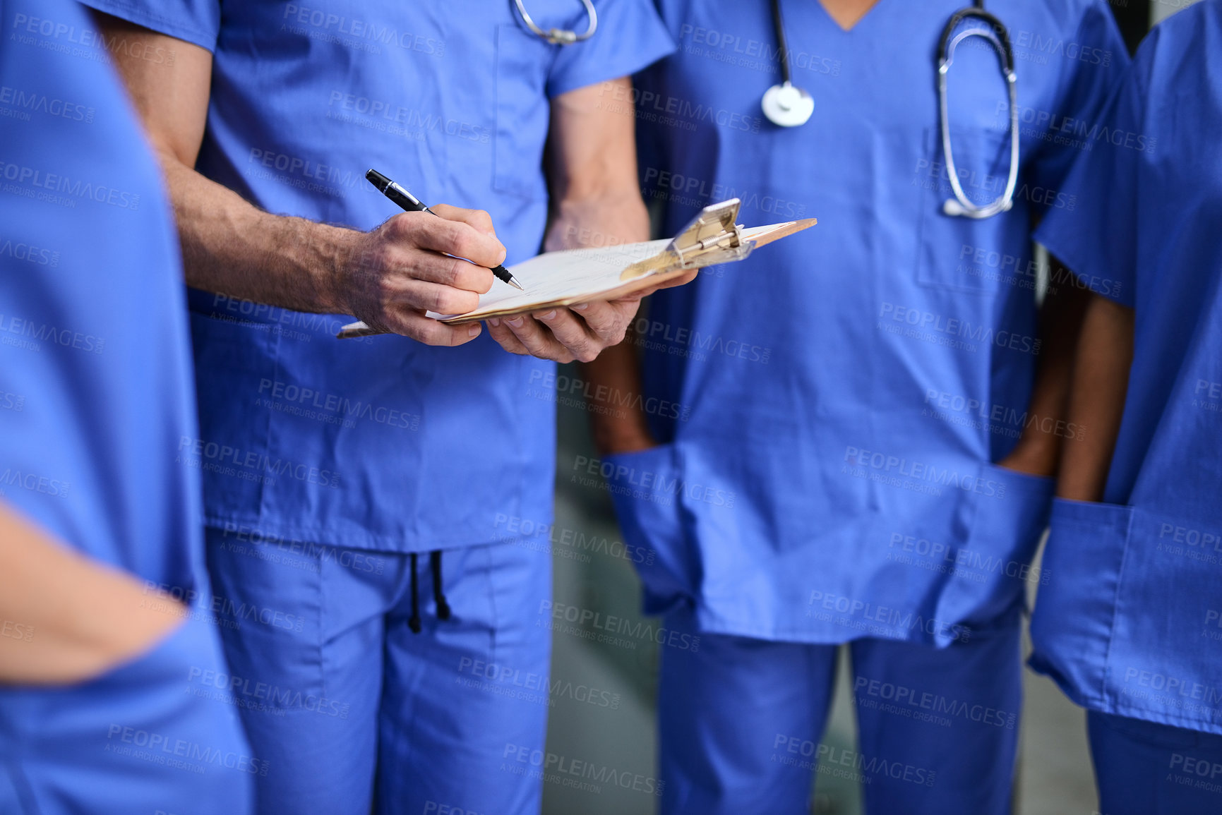Buy stock photo Cropped shot of a medical practitioner writing notes on a clipboard with colleagues around