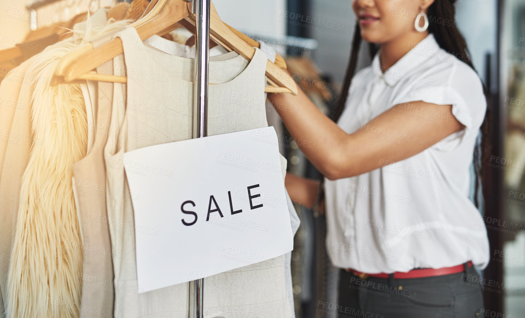 Buy stock photo Cropped shot of an unidentifiable woman rearranging clothes on a rail with a sign that reads 