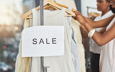 Buy stock photo Cropped shot of two women looking at dresses on a rail with a sign that reads 