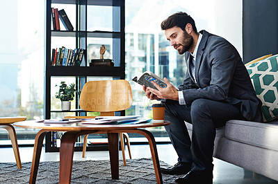Buy stock photo Shot of a young businessman reading a book in a modern office