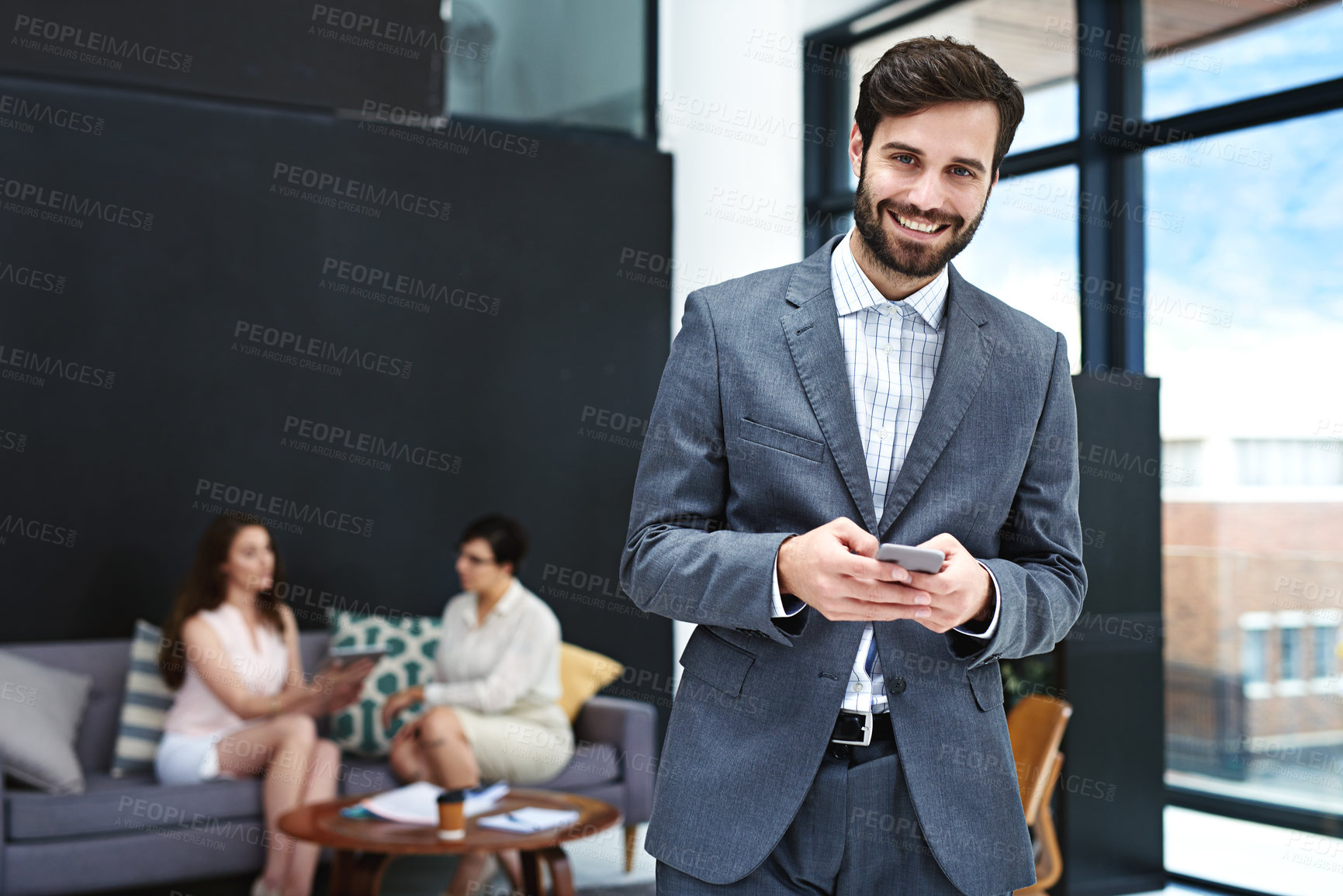 Buy stock photo Portrait of a young businessman texting on a cellphone with colleagues in the background