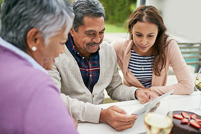 Buy stock photo Cropped shot of a senior man showing his family something on his tablet as they have lunch outside