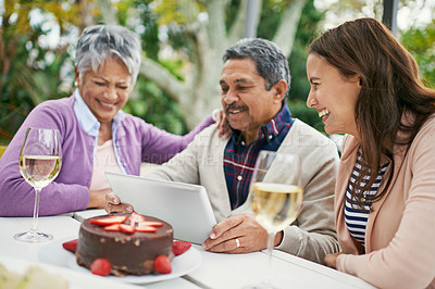 Buy stock photo Cropped shot of a senior man showing his family something on his tablet as they have lunch outside