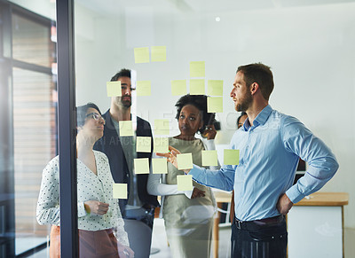 Buy stock photo Cropped shot of a group of businesspeople working on a glass wall in the office