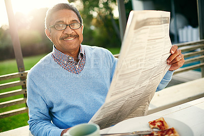 Buy stock photo Portrait of a happy older man reading a newspaper with his breakfast outdoors