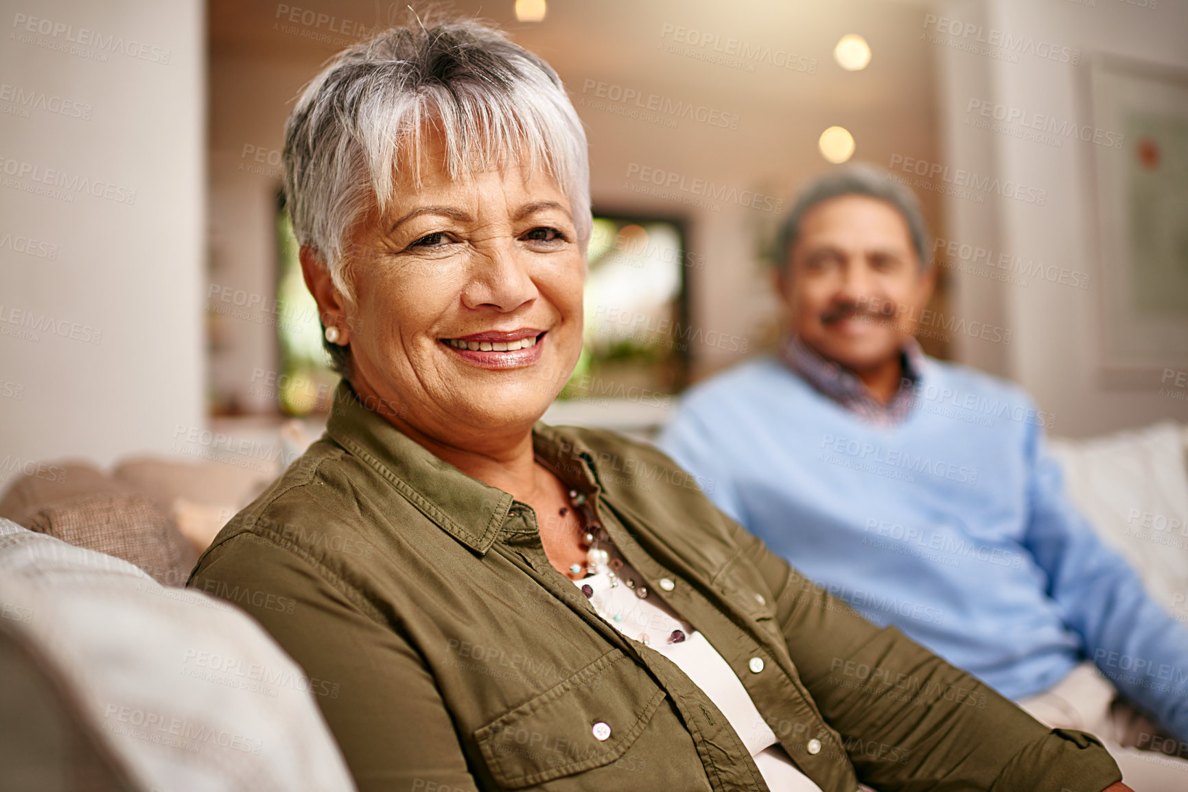 Buy stock photo Portrait of a happy older woman relaxing on the sofa with her husband in the background
