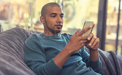 Buy stock photo Shot of a young man relaxing on a beanbag and using a mobile phone