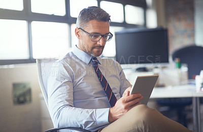 Buy stock photo Cropped shot of a businessman using his digital tablet while sitting in his office