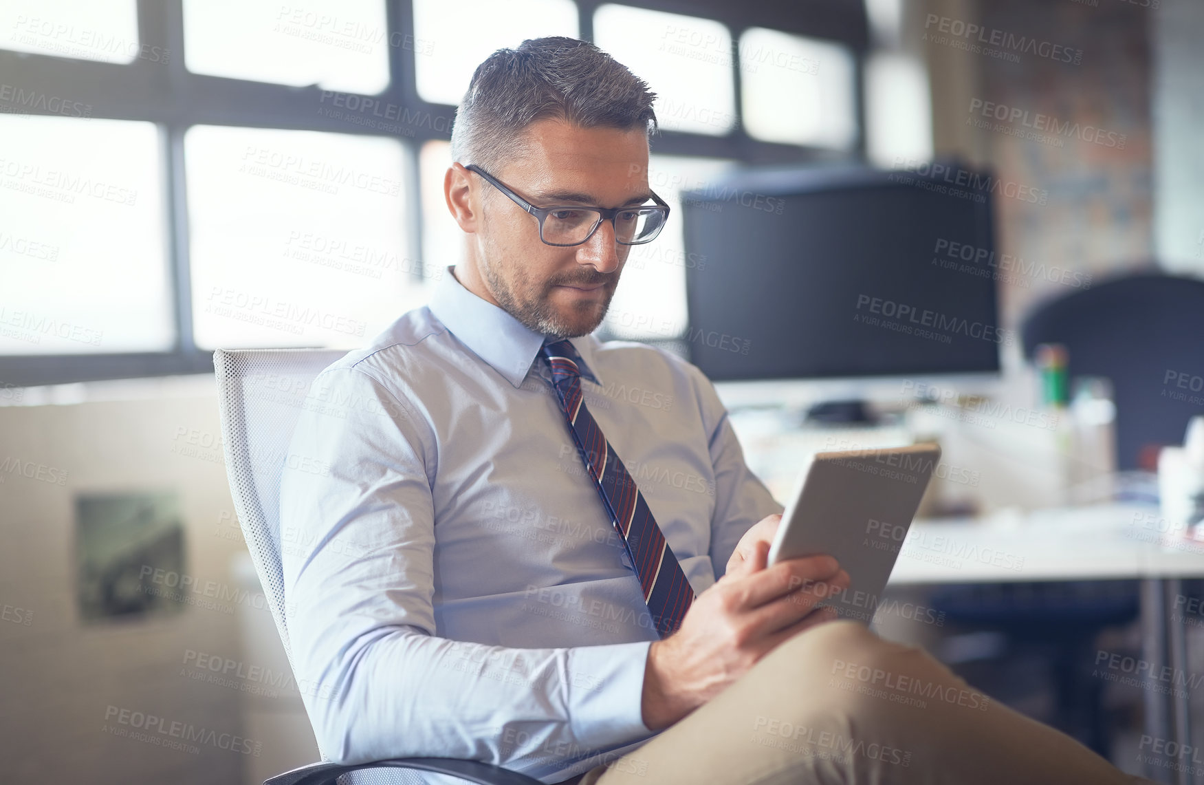 Buy stock photo Cropped shot of a businessman using his digital tablet while sitting in his office