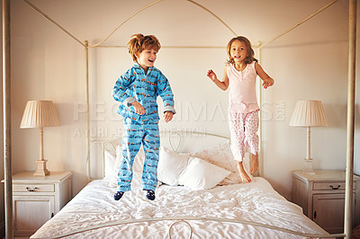 Buy stock photo Shot of two young children jumping together on a bed at home