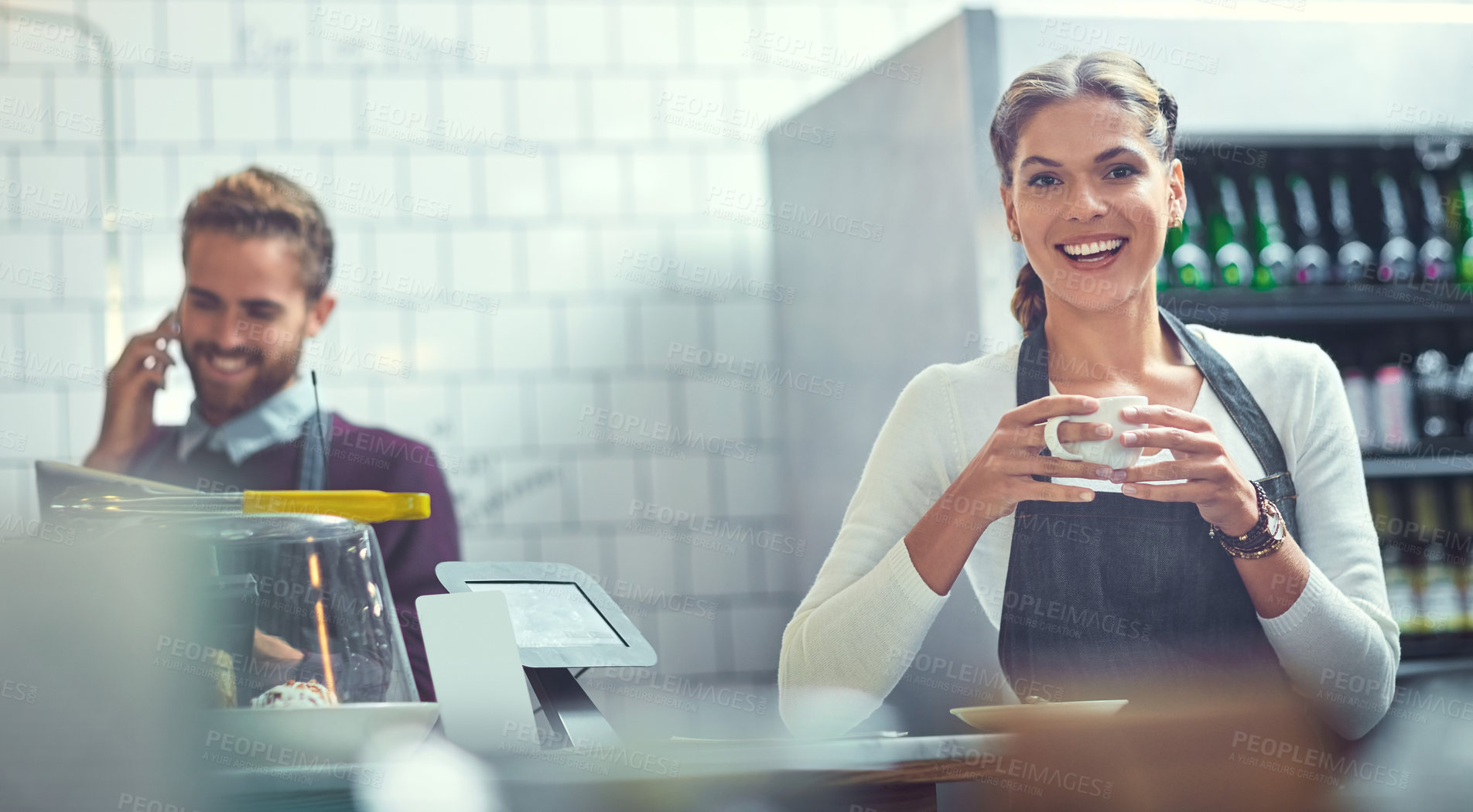 Buy stock photo Portrait of a young woman having coffee in a store while her coworker works in the background