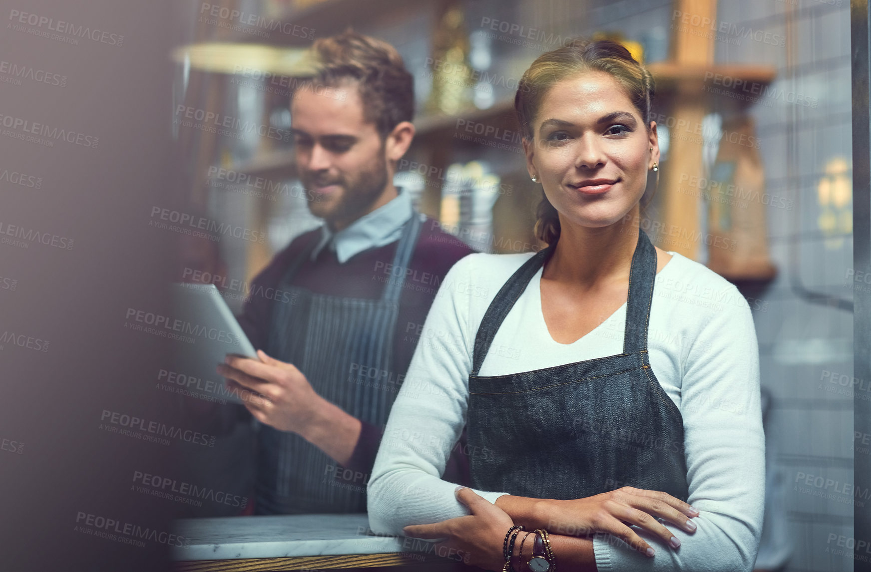 Buy stock photo Portrait of a young woman working in a store while her coworker uses a digital tablet in the background