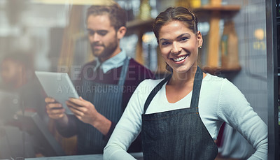 Buy stock photo Portrait of a young woman working in a store while her coworker uses a digital tablet in the background