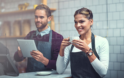 Buy stock photo Shot of a young woman having coffee in a store while her coworker works in the background