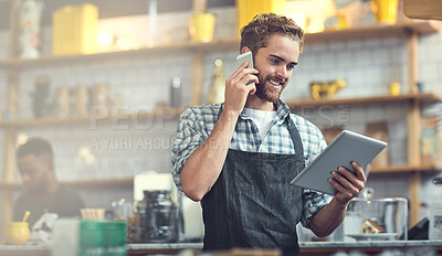 Buy stock photo Shot of a young man using a phone and digital tablet in the store that he works at
