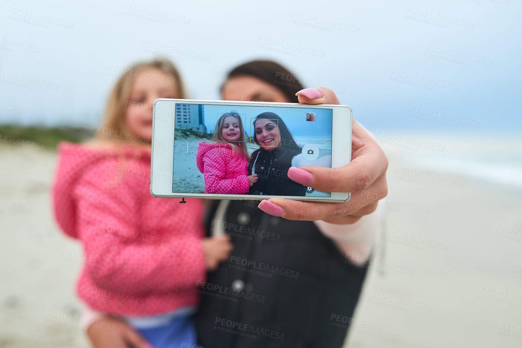 Buy stock photo Cropped shot of a mother and her young daughter taking a selfie on the beach