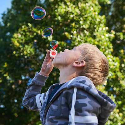 Buy stock photo Shot of a cute young boy blowing bubbles outside