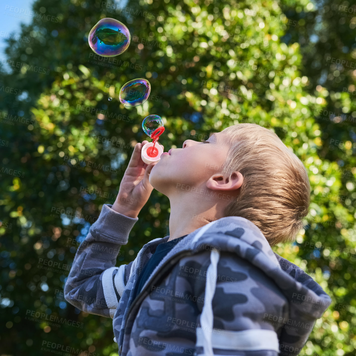 Buy stock photo Shot of a cute young boy blowing bubbles outside