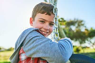 Buy stock photo Portrait of a young boy sitting on a swing in a park