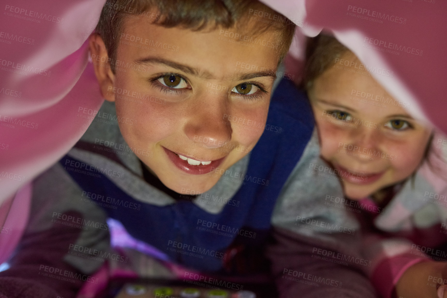 Buy stock photo Portrait of two young siblings lying down under a blanket at home