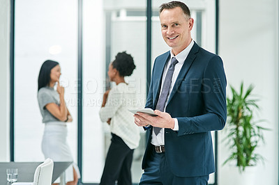 Buy stock photo Cropped portrait of a mature businessman looking at a tablet in the office with his colleagues in the background