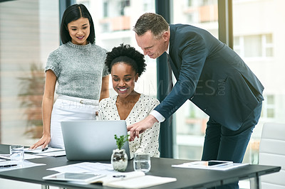 Buy stock photo Cropped shot of three businesspeople gathered around a laptop in the office