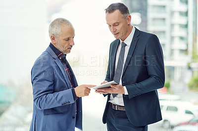 Buy stock photo Cropped shot of two businessmen working on a digital tablet together in a modern office