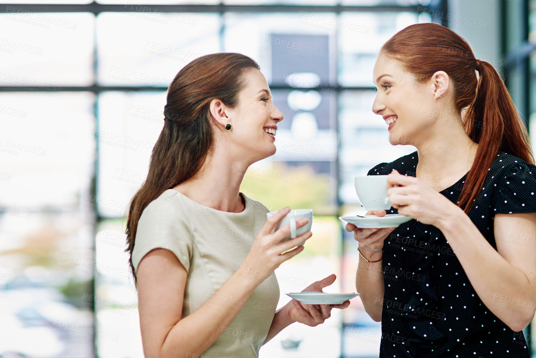 Buy stock photo Cropped shot of two businesswomen standing and chatting during a coffee break