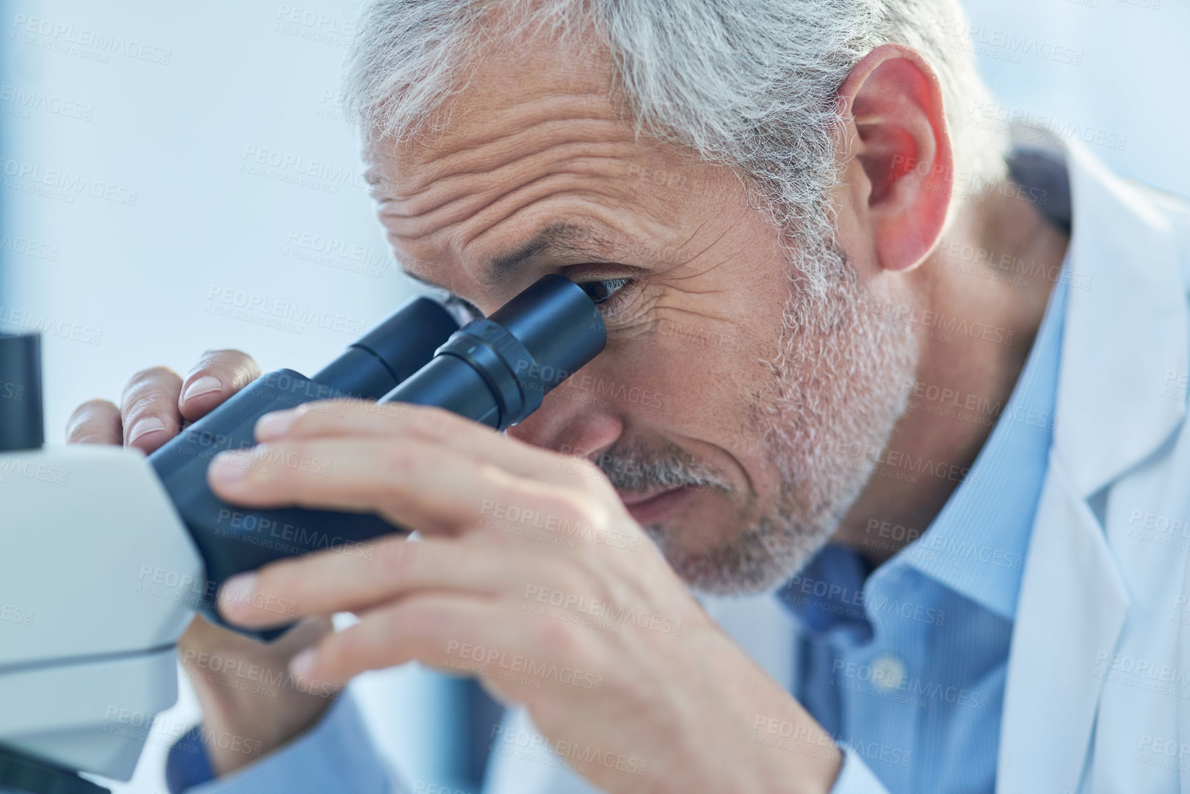 Buy stock photo Closeup shot of a male scientist looking through a microscope in a lab
