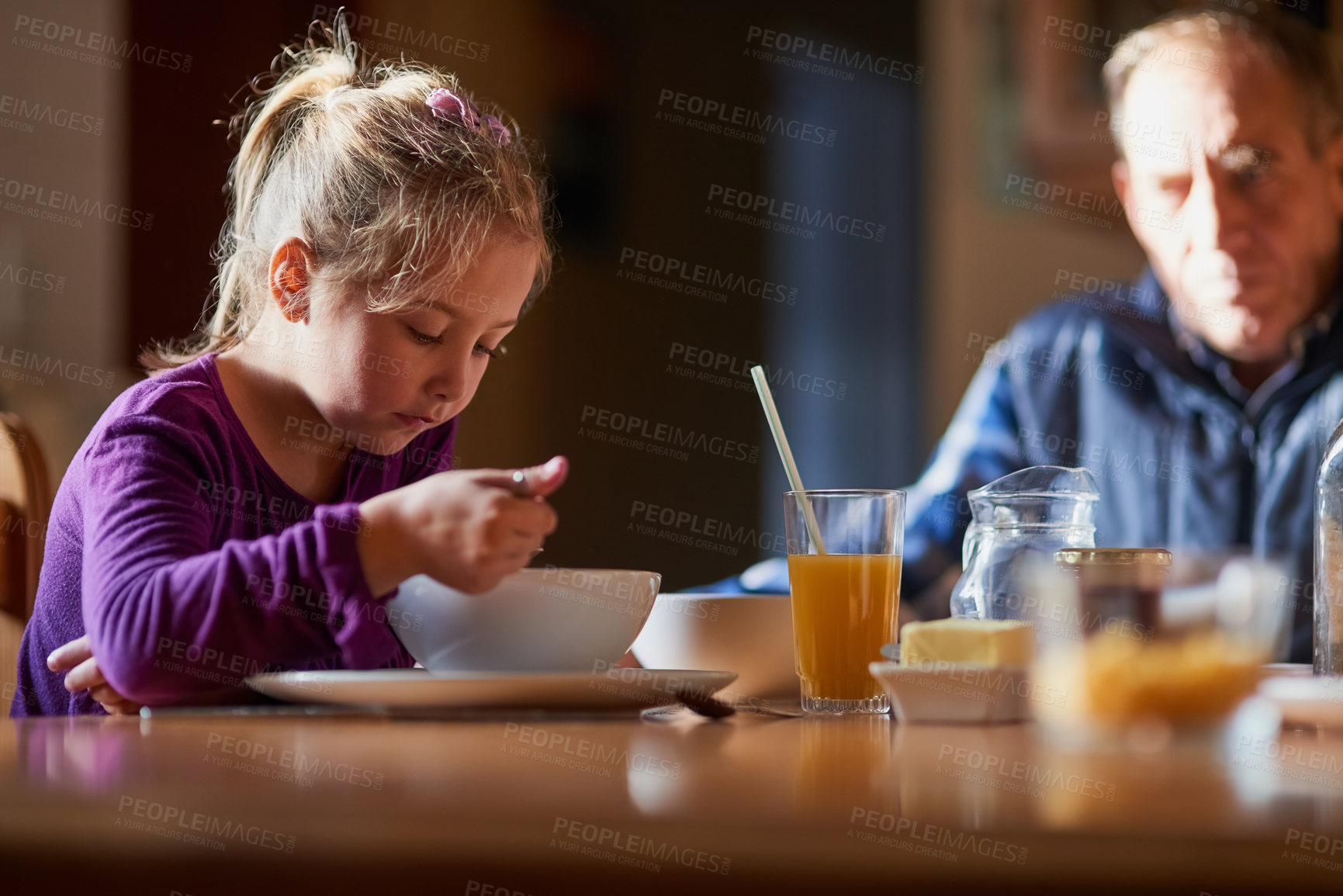 Buy stock photo Cropped shot of a young girl eating cereal at the table with her grandfather in the background