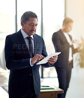 Buy stock photo Cropped shot of a mature business using his tablet while standing in the office