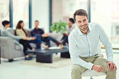 Buy stock photo Portrait of a confident young businessman sitting in an office with colleagues in the background