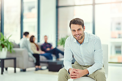 Buy stock photo Portrait of a confident young businessman sitting in an office with colleagues in the background