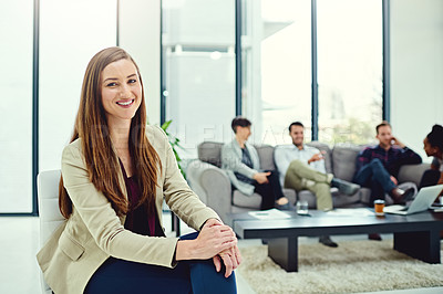 Buy stock photo Portrait of a confident young businesswoman sitting in an office with colleagues in the background
