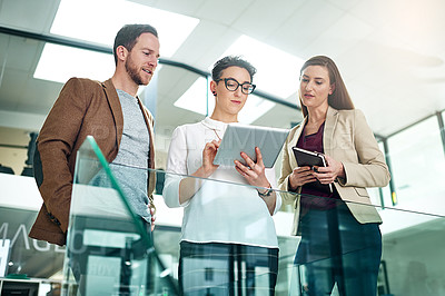 Buy stock photo Shot of a group of colleagues talking together over a digital tablet while standing in a large modern office