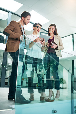 Buy stock photo Shot of a group of colleagues talking together over a digital tablet while standing in a large modern office