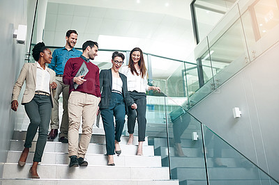 Buy stock photo Shot of a group of colleagues talking together while walking down stairs in a large modern office