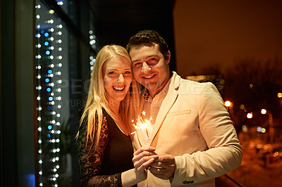 Buy stock photo Cropped portrait of a couple standing with sparklers on a balcony during a party