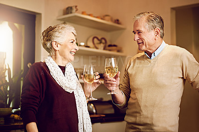 Buy stock photo Shot of an elderly couple chatting and drinking wine together while standing in their kitchen