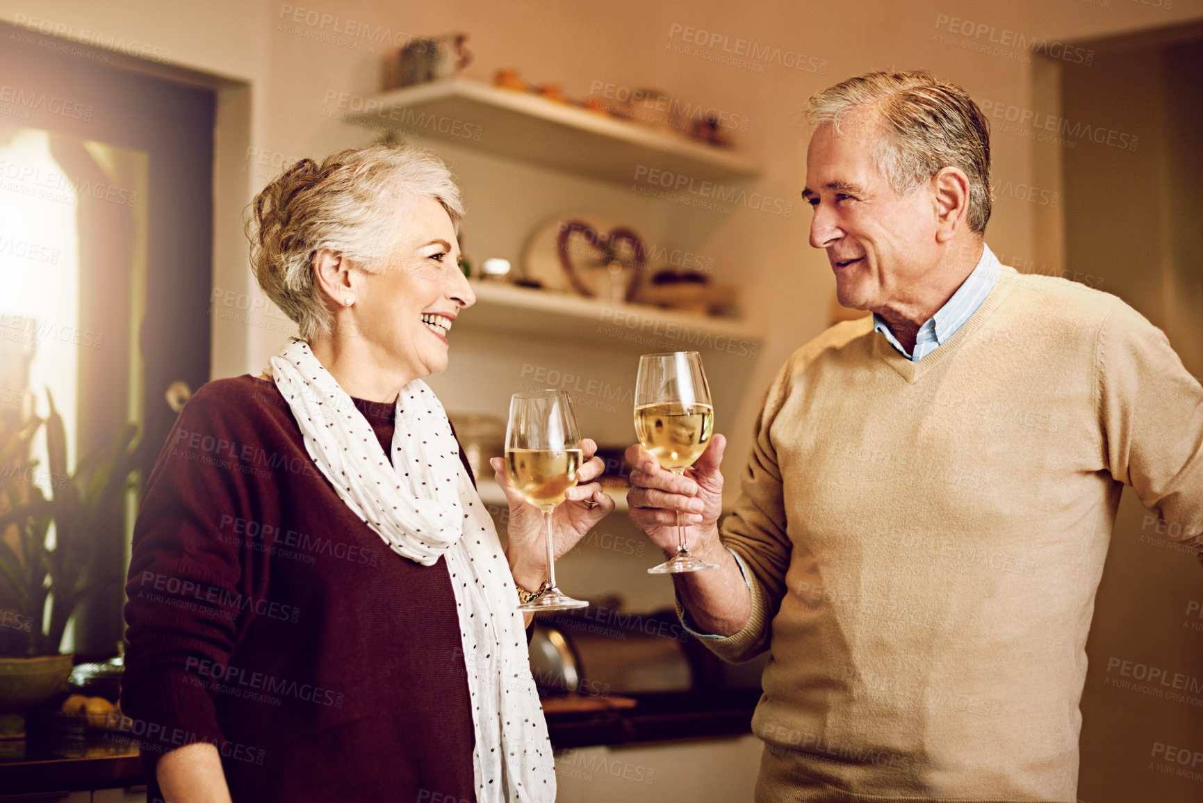 Buy stock photo Shot of an elderly couple chatting and drinking wine together while standing in their kitchen