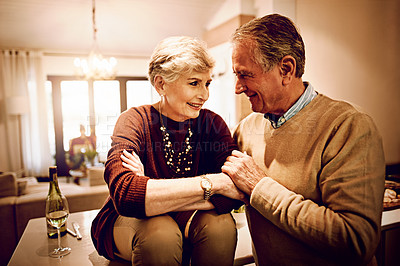 Buy stock photo Shot of an elderly couple chatting and drinking wine together in their kitchen