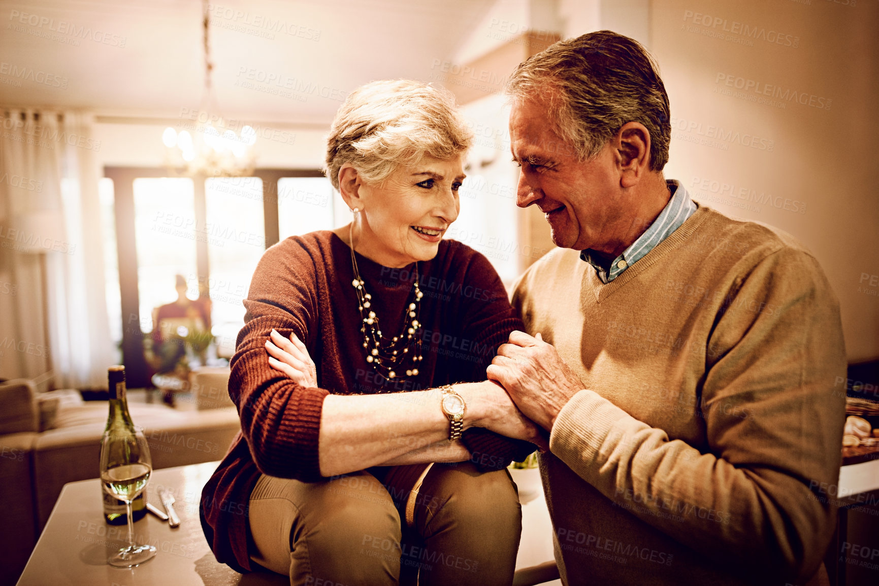 Buy stock photo Shot of an elderly couple chatting and drinking wine together in their kitchen