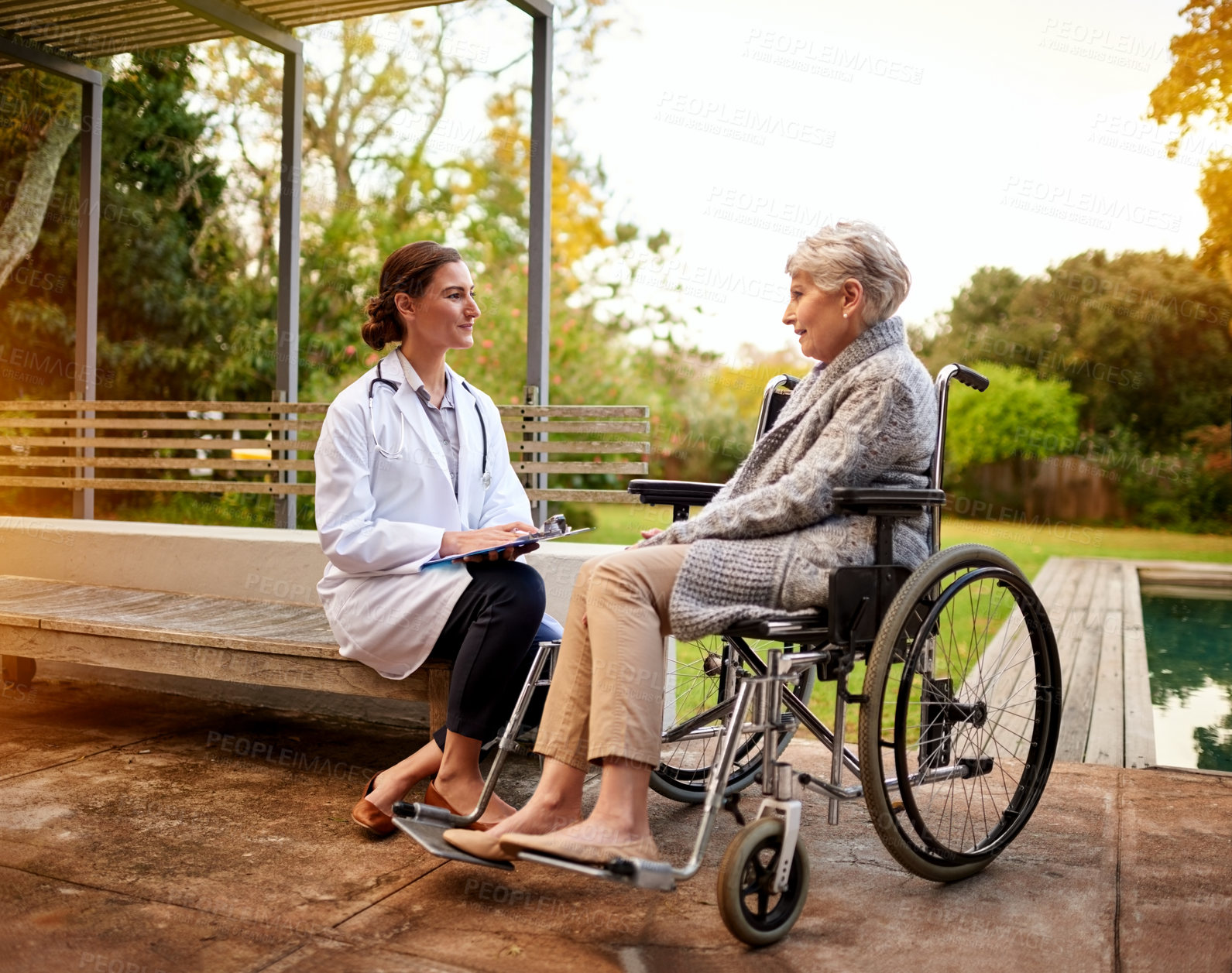 Buy stock photo Shot of a young doctor and her elderly patient talking while sitting outside