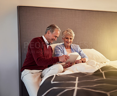 Buy stock photo Cropped shot of a senior couple looking at a tablet together while sitting in bed
