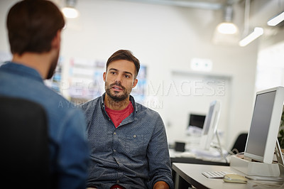 Buy stock photo Shot of two young businessmen talking together at a desk in an office